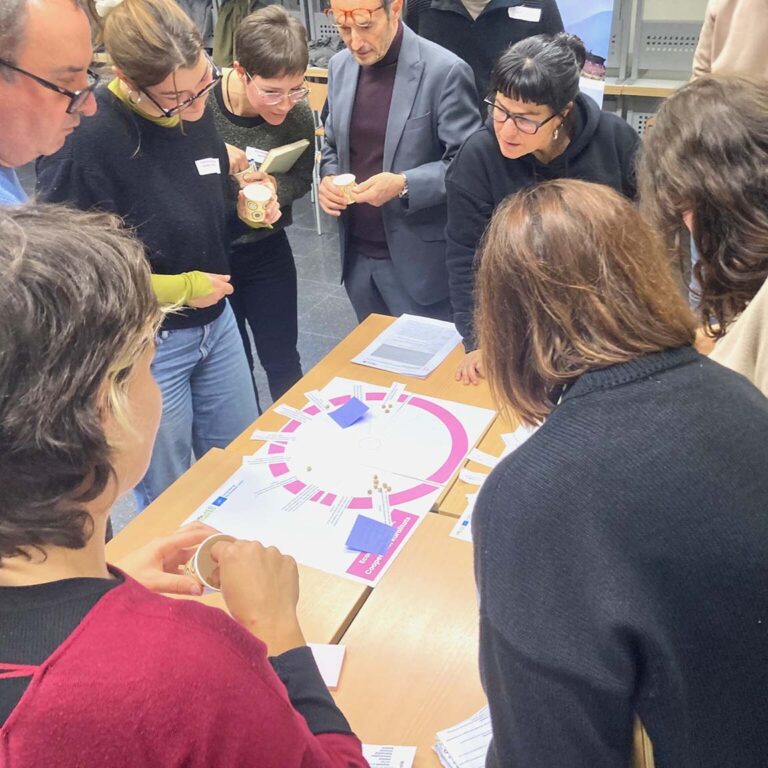 Group of people gathered around a table interacting with a game or graphic co-creation tool, in a collaborative work environment.